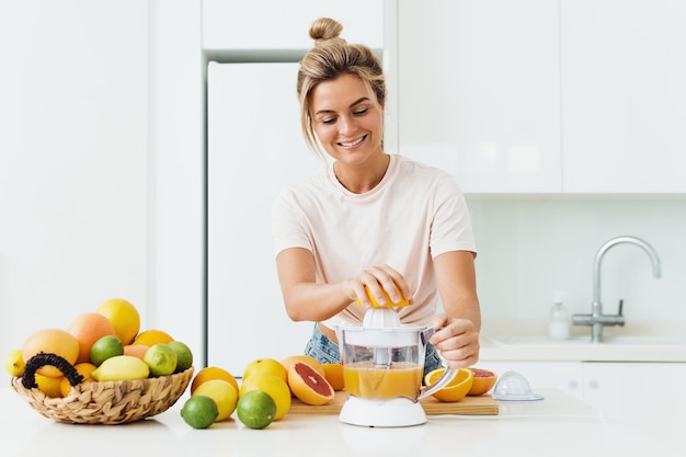 Donna allegra con molti agrumi durante la preparazione del succo d'arancia fresco a casa