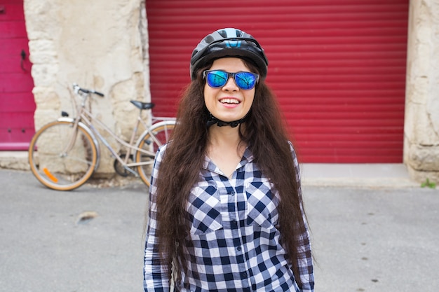 Donna allegra con occhiali da sole e casco sullo sfondo porta rossa e bicicletta