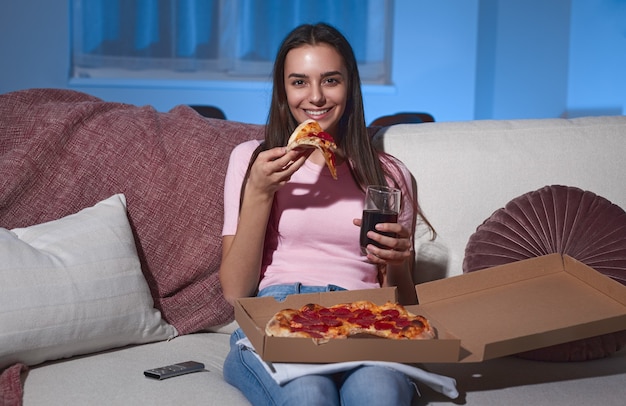 Donna allegra con pizza e drink guardando film