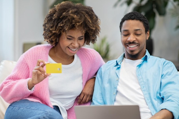 Donna allegra dell'uomo di colore che utilizza la carta di credito del computer portatile a casa