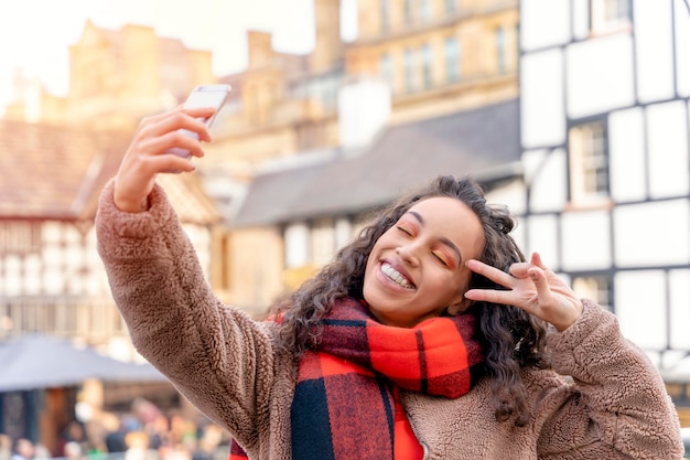 Donna allegra di etnia mista che prende selfie sullo smartphone sorridendo e viaggiando in Europa