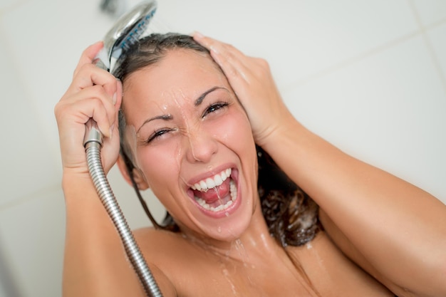 Donna allegra doccia che lava viso e capelli mentre fa la doccia sotto la testa della doccia.