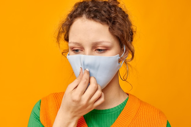 Donna allegra in una maglietta gialla protezione maschera medica sfondo rosa inalterato