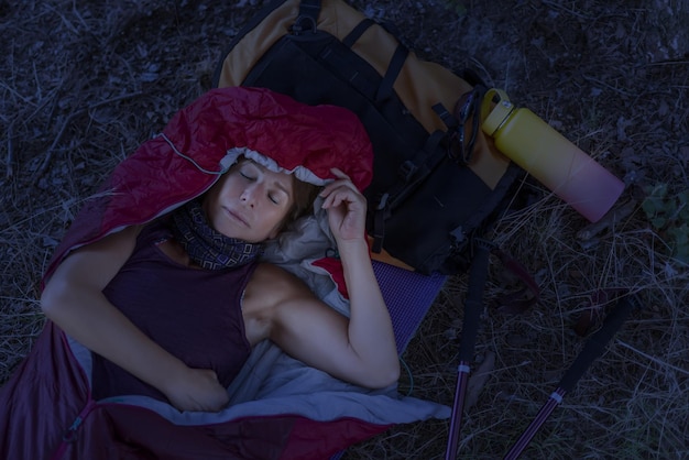 Donna alpinista che dorme in un sacco a pelo al calar della notte in estate usando il suo zaino come cuscino