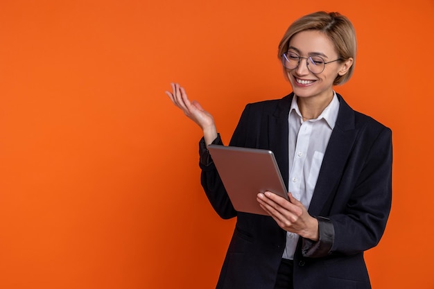 Donna amichevole che indossa un abito nero in stile ufficiale videoconferenza su tablet isolata su sfondo arancione