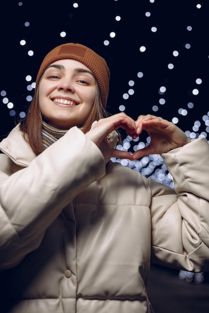 donna amorevole che mostra il gesto del cuore per le vacanze di San Valentino mentre si trova nella città d'inverno