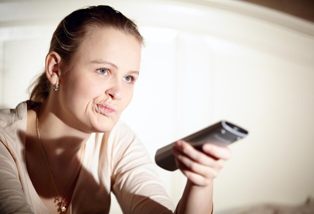 Donna annoiata che fa la faccia mentre tiene in mano il telecomando a casa