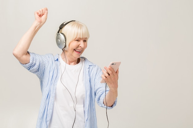 Donna anziana allegra con le cuffie che ascolta la musica su un telefono isolato su priorità bassa bianca.