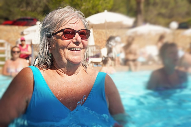 Donna anziana anziana con i capelli grigi, che indossa un costume da bagno blu che fa aerobica in acqua nella piscina dell'hotel