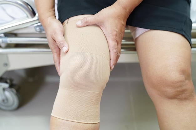 Donna anziana asiatica che indossa una protesi elastica per il ginocchio per ridurre il dolore