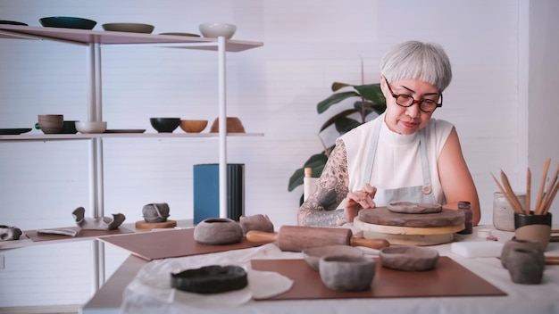 Donna anziana asiatica che si gode il lavoro di ceramica a casa Una ceramista femminile sta realizzando nuove ceramiche in uno studio