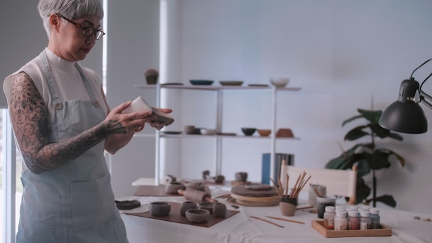 Donna anziana asiatica che si gode il lavoro di ceramica a casa Una ceramista femminile sta realizzando nuove ceramiche in uno studio