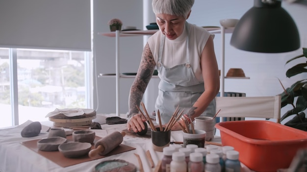 Donna anziana asiatica che si gode il lavoro di ceramica a casa Una ceramista femminile sta realizzando nuove ceramiche in uno studio