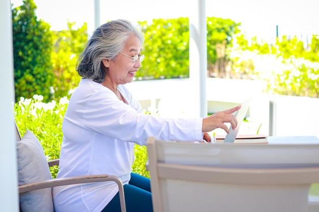 Donna anziana asiatica che si rilassa a casa giocando con il computer portatile in chat online con gli amici Il concetto di vivere in pensione per essere felice