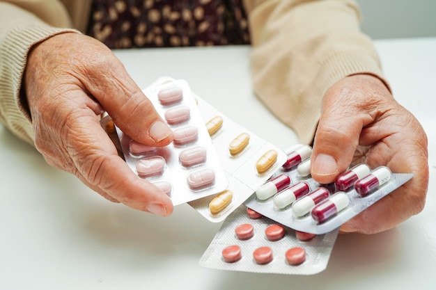 Donna anziana asiatica che tiene la pillola farmaco in mano forte concetto medico sano