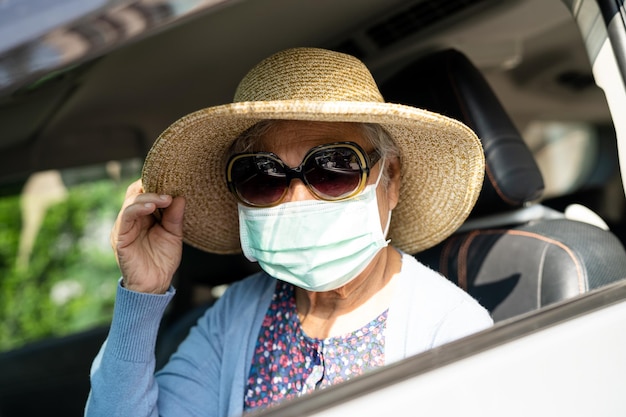Donna anziana asiatica con cappello seduta in macchina con divertimento e libertà nel viaggio