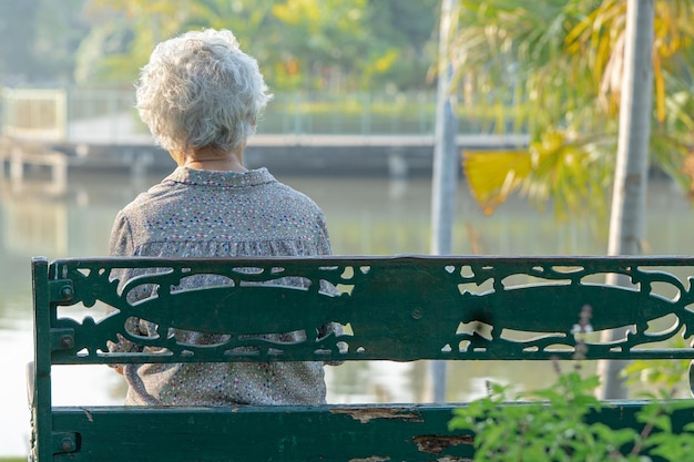 Donna anziana asiatica depressa e triste che si siede indietro sulla panchina nel parco autunnale.