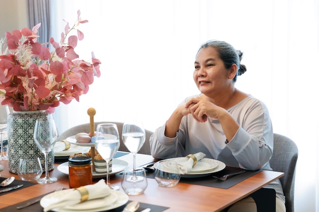 Donna anziana asiatica sorridente che aspetta il cibo per la colazione sedendosi al tavolo da pranzo a casa