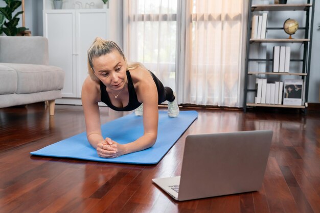 Donna anziana atletica e sportiva che plana sul tappetino per esercizi fitness mentre guardi video di fitness online a casa come concetto di stile di vita sano e in forma dopo il pensionamento