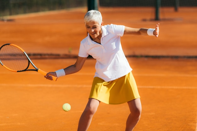 Donna anziana attiva sui sessant'anni che gioca a tennis ricreativo