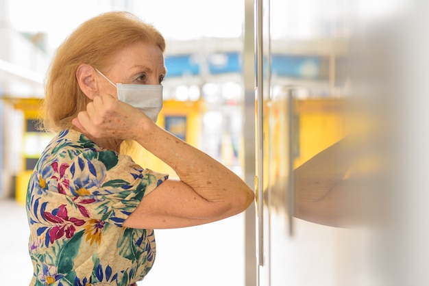 Donna anziana bionda con maschera che preme il pulsante dell'ascensore con il gomito per evitare di diffondere il coronavirus covid-19