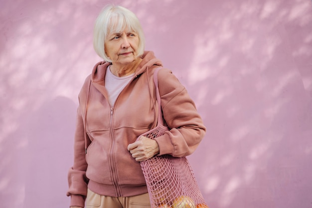 donna anziana calma in felpa con cappuccio accogliente che trasporta un sacco di cotone con la spesa