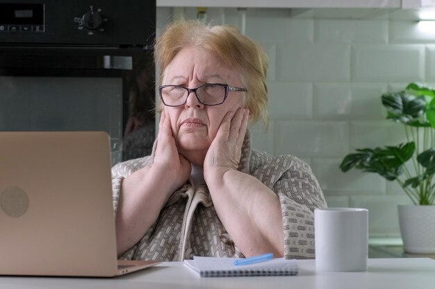 Donna anziana caucasica preoccupata a casa che guarda il computer portatile che vede cattive notizie