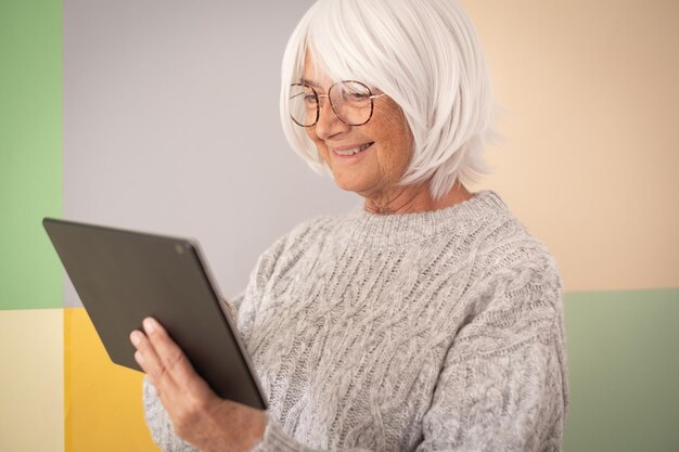 Donna anziana caucasica sorridente che utilizza tablet digitale isolato su sfondo colorato spazio copia