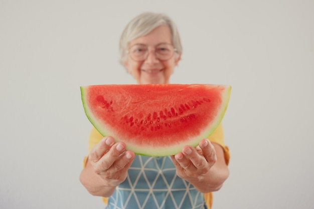 Donna anziana caucasica sorridente sfocata che tiene una fetta di anguria fresca guardando il concetto di stile di vita mangiare sano della fotocamera