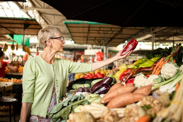 Donna anziana che acquista verdure biologiche fresche al mercato per un nutrimento sano.