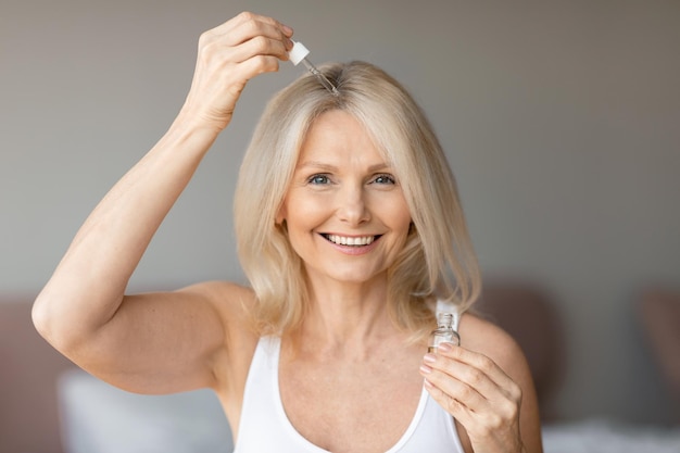 Donna anziana che applica siero di riparazione o olio naturale sui capelli utilizzando cosmetici biologici coccole