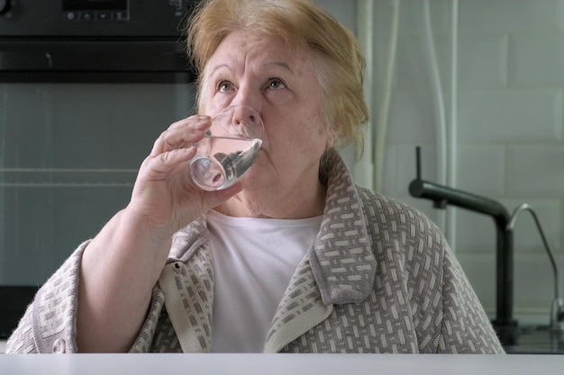 Donna anziana che beve acqua dal vetro in cucina a casa