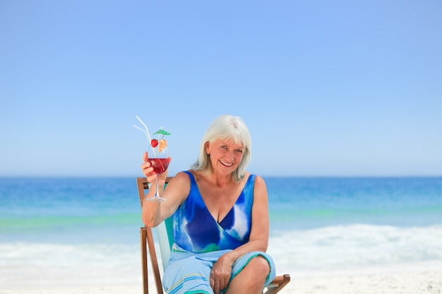 Donna anziana che beve un cocktail sulla spiaggia