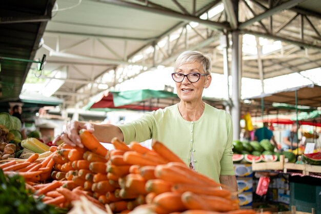 donna anziana che compra frutta e verdura fresca al mercato e tiene in mano una borsa piena di cibo sano