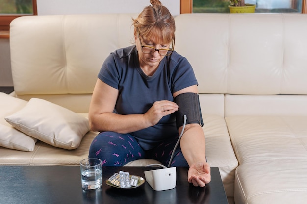 Donna anziana che controlla il livello di pressione sanguigna a casa donna anziana che soffre di pressione alta seduta su un divano e utilizza un tonometro pulsometro
