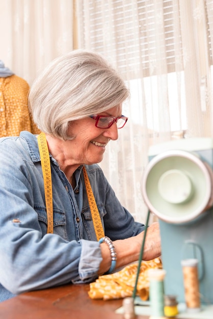 Donna anziana che cuce davanti a una macchina da cucire con un'espressione di felicità