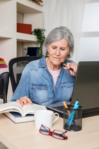 Donna anziana che esamina un libro davanti a un computer su una scrivania