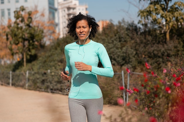 Donna anziana che fa jogging all'aperto con smartphone e auricolari