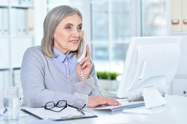Donna anziana che lavora al computer e parla al telefono