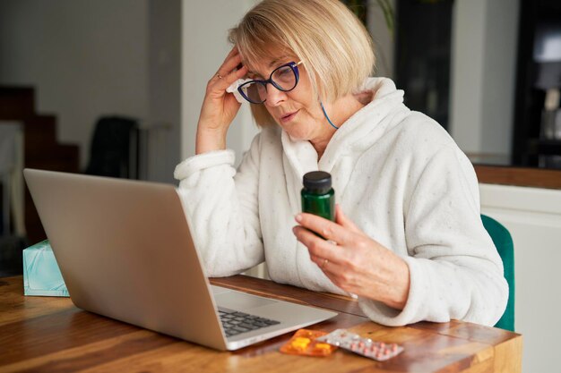 Donna anziana che mostra la medicina durante la consultazione online a casa