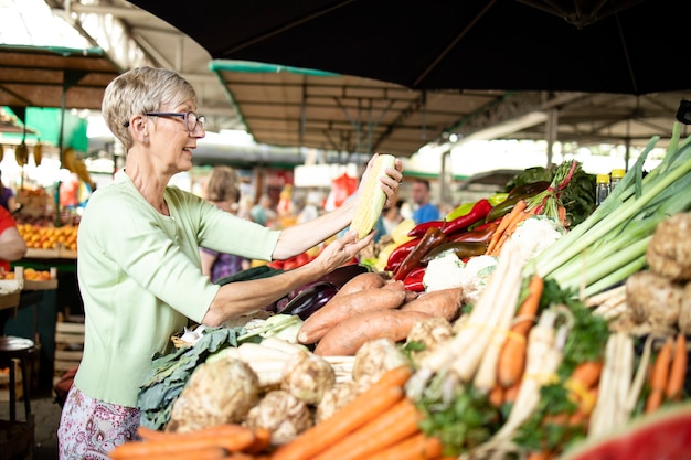 Donna anziana che sceglie e acquista verdure sane nella piazza del mercato.