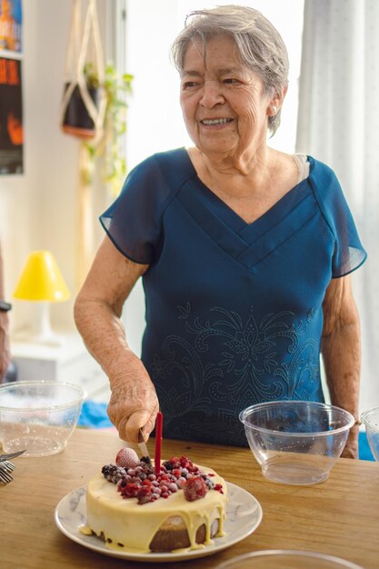 Donna anziana che taglia la sua torta gelato di compleanno con bacche rosse Foto verticale