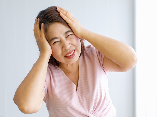 Donna anziana che usa le mani per afferrare e tenere la testa con dolore e soffre di viso deformato da mal di testa con malattia cerebrovascolare o colpo alla testa.