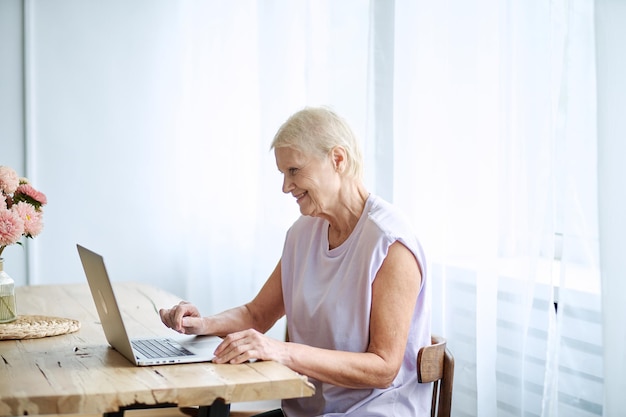 Donna anziana che utilizza un computer portatile in un soggiorno accogliente