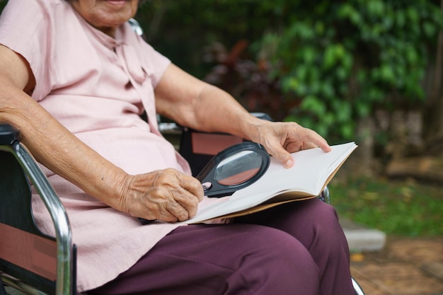 Donna anziana che utilizza una lente d'ingrandimento per leggere sulla sedia a rotelle.