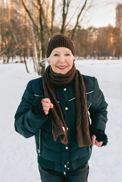 donna anziana con cappello e giacca sportiva che fa jogging nella neve invernale park
