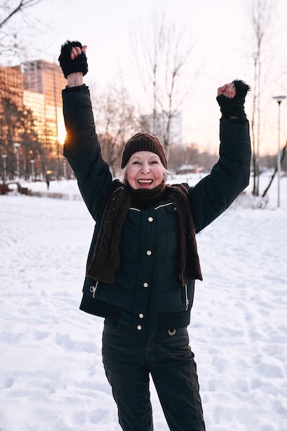 donna anziana con cappello e giacca sportiva che fa jogging nella neve invernale park