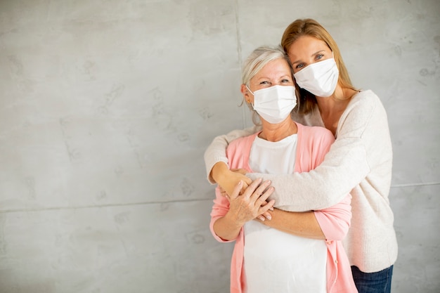 Donna anziana con figlia premurosa a casa che indossa maschere mediche come protezione dal coronavirus