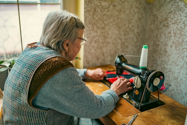 Donna anziana con gli occhiali usa la macchina da cucire mani rugose della vecchia sarta donna anziana Vecchia macchina da cucire Macchina da cucire manuale classica in stile retrò pronta per il lavoro di cucito