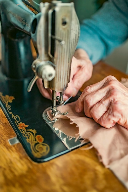 Donna anziana con gli occhiali usa la macchina da cucire mani rugose della vecchia sarta donna anziana Vecchia macchina da cucire Macchina da cucire manuale classica in stile retrò pronta per il lavoro di cucito